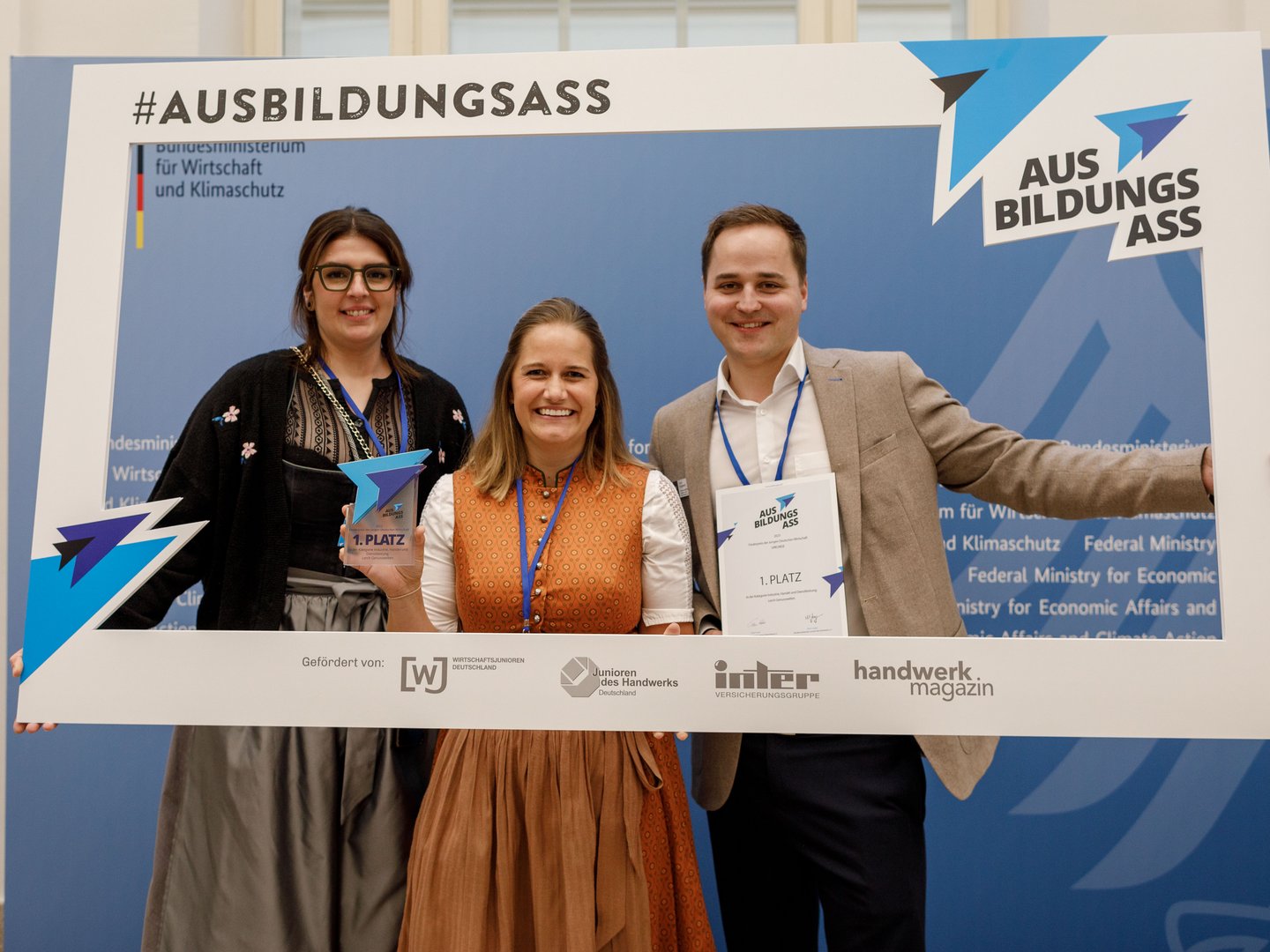 Auszeichnungen unserer Berghütte mit Sauna im Allgäu Drei Personen halten einen großen Rahmen mit dem Text Ausbildungsass und Preisen