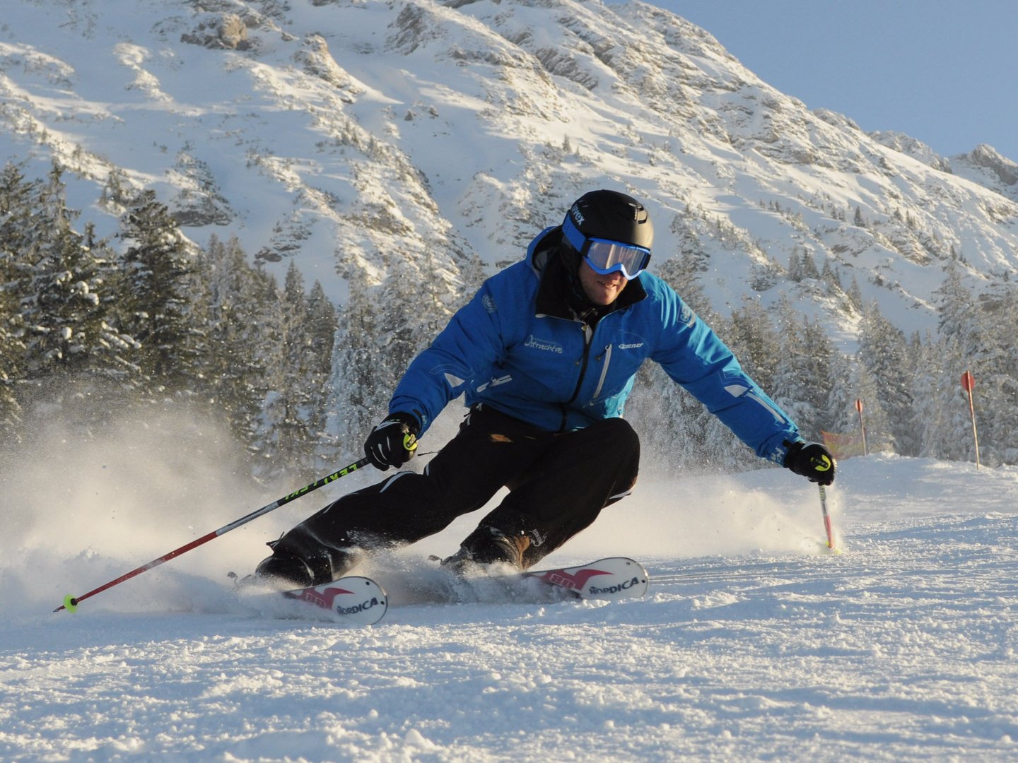 Skifahren lernen im Herzen des Allgäus Skifahrer in blauer Jacke fährt auf verschneiter Piste vor Bergkulisse