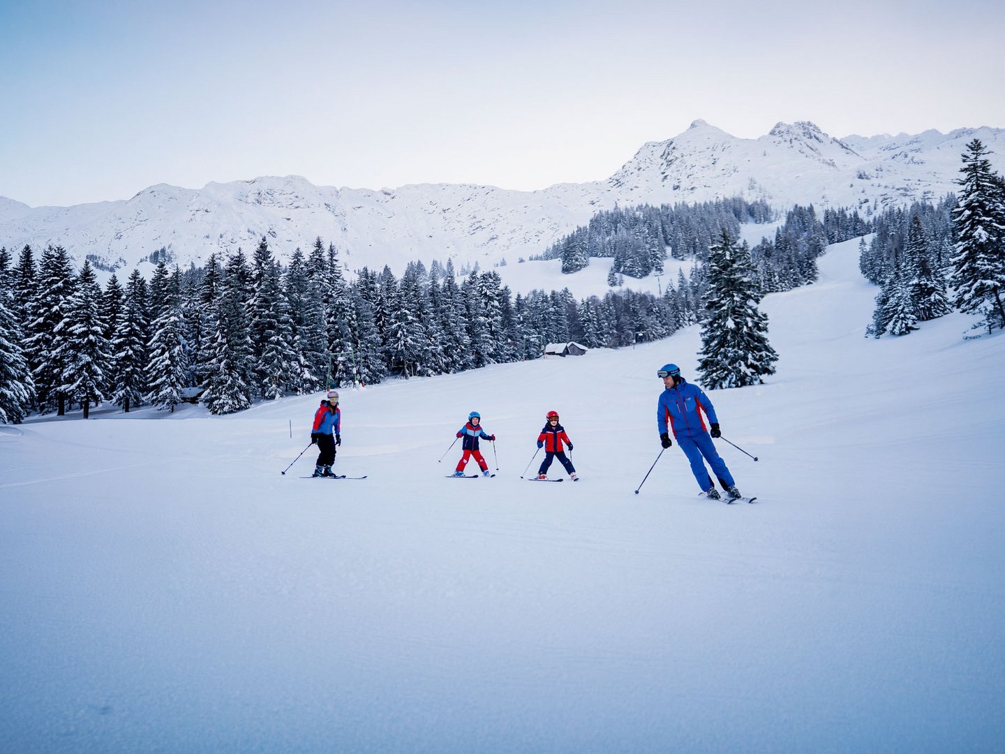 Skifahren lernen im Herzen des Allgäus Vier Skifahrer auf einer verschneiten Piste vor bewaldeten Bergen